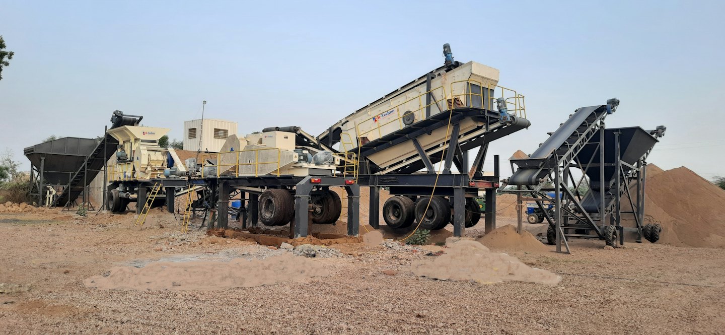 Outdoor industrial rock crushing plant with conveyors and aggregate piles.