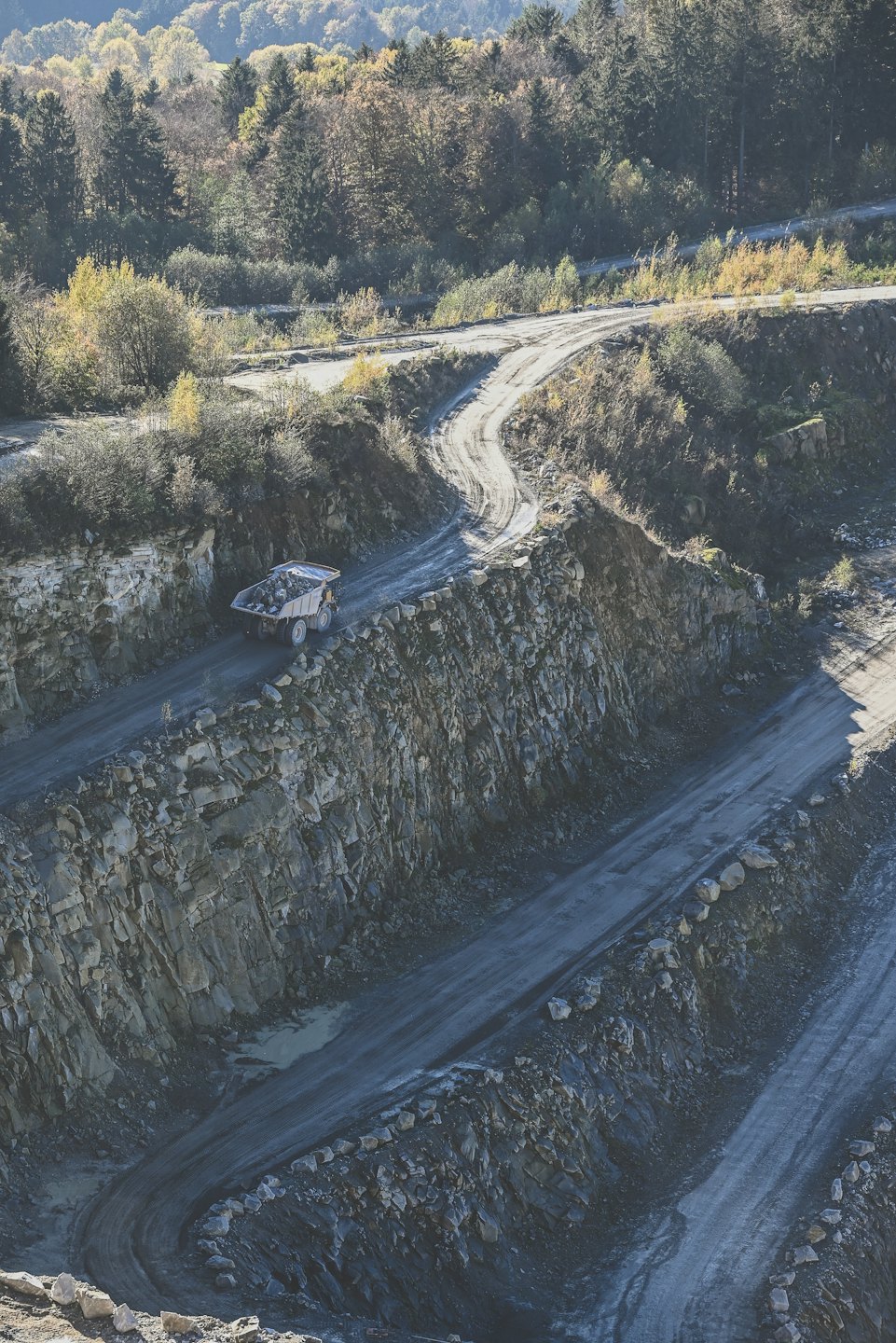 Articulated dump truck hauls rocks on a winding quarry road.