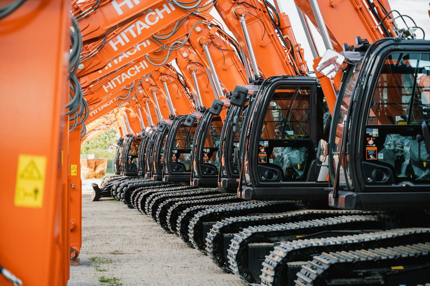 New orange and black Hitachi excavators lined up on gravel.
