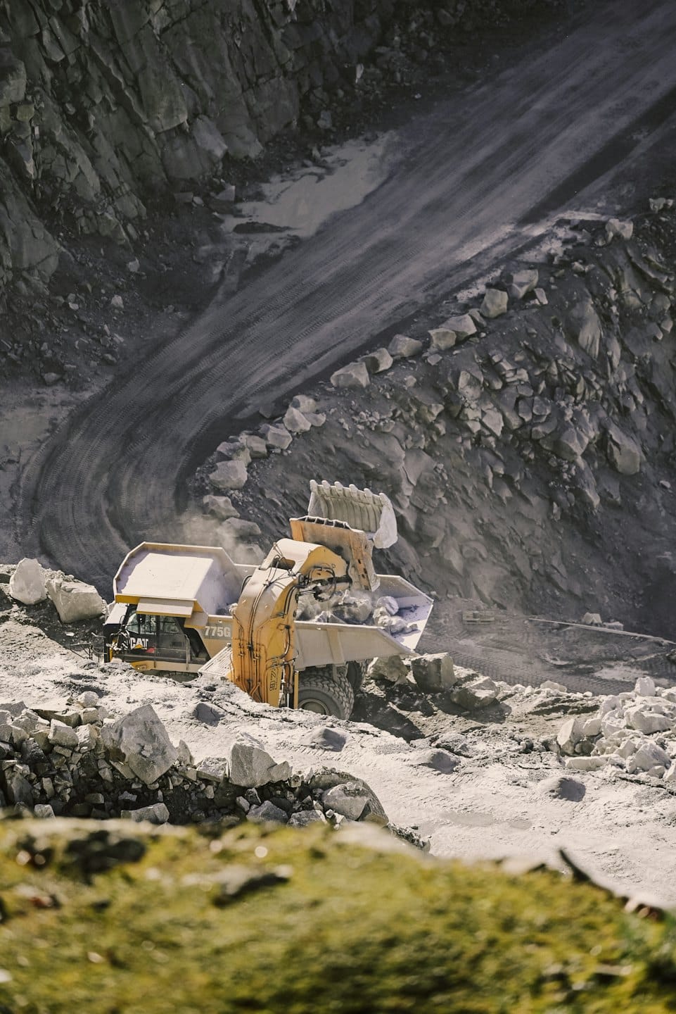 Yellow excavator loads rock into a dump truck in a quarry.